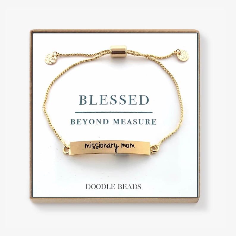 May include: Gold adjustable bracelet with a small rectangular charm that reads "missionary mom". The bracelet is in a box with the words "Blessed Beyond Measure" and "Doodle Beads" printed on it.