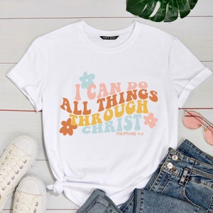 May include: White t-shirt with a colorful graphic that says "I can do all things through Christ" with flowers and the scripture reference "Philippians 4:13".