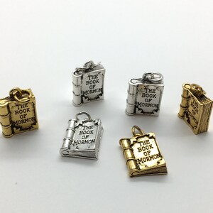 May include: Five silver and gold charms shaped like closed books with the words "The Book of Mormon" inscribed on them.