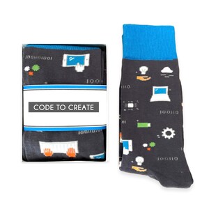 May include: A pair of black socks with a blue cuff. The socks feature a pattern of computer-related icons, including a computer, a keyboard, a mouse, a lightbulb, and a cloud. The socks also have the text "CODE TO CREATE" on the packaging.