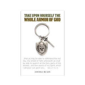 May include: A silver keychain with a shield and sword charm. The shield has a fleur-de-lis design. The keychain has the text "Take upon yourself the whole armor of God... that ye may be able to withstand the evil day... the shield of faith wherewith ye shall be able to quench all the fiery darts of the wicked... and the sword of my Spirit, which I will pour out upon you... D&C 27:15-18" and "Doodle Beads".