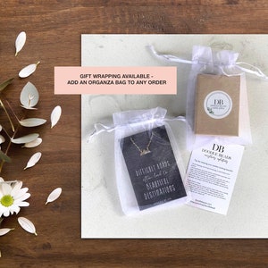 Pode incluir: Um colar de prata com um pingente de cordilheira montanhosa em um cart&atilde;o preto com o texto "Difficult roads often lead to beautiful destinations". O colar est&aacute; embalado em uma bolsa de organza branca com uma caixa marrom e um cart&atilde;o com o texto "Doodle Beads Jewelry".
