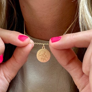 May include: A gold necklace with a round pendant featuring a detailed engraved design of two figures embracing.