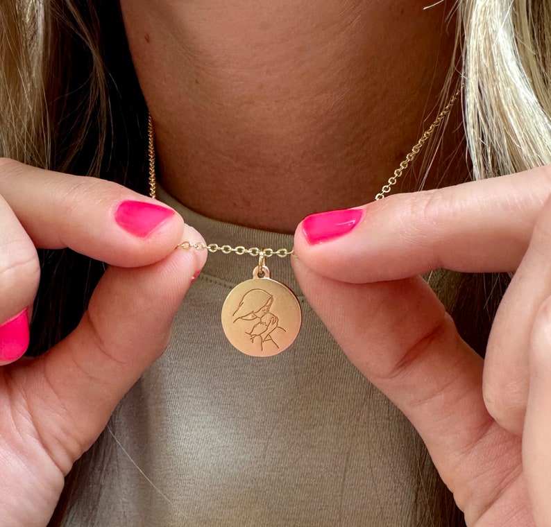 May include: A gold necklace with a round pendant featuring a detailed engraved design of two figures embracing.