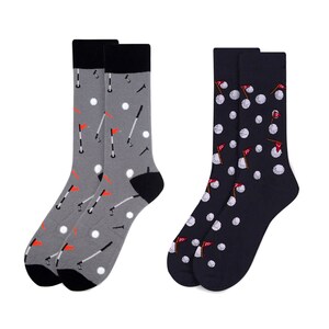 May include: Two pairs of socks with a golf theme. One pair is gray with white golf balls, red flags, and golf clubs. The other pair is navy blue with white golf balls and red flags.