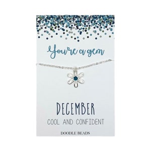 May include: A silver necklace with a blue gemstone flower pendant. The card reads "You're a gem" and "December Cool and Confident" with the Doodle Beads logo.