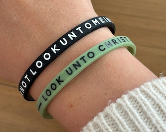 Puede incluir: Dos pulseras de silicona con el texto "Look unto me" y "Look unto Christ" en letras blancas.