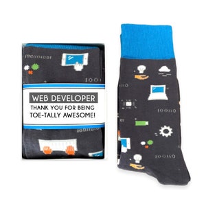 May include: A gift box containing a pair of black socks with a blue cuff. The socks feature a pattern of computer-related icons, including a laptop, a lightbulb, a cloud, and binary code. The box has a white label with the text "WEB DEVELOPER THANK YOU FOR BEING TOE-TALLY AWESOME!"