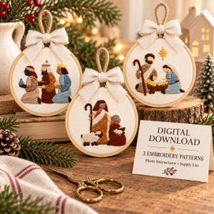 May include: Three circular embroidery hoops featuring nativity scenes with figures stitched in thread on white fabric. Each hoop is topped with a beige ribbon bow and a jute hanging loop. A card reads: DIGITAL DOWNLOAD 3 EMBROIDERY PATTERNS.