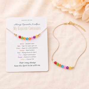 May include: A beaded necklace with colorful beads and gold accents. The necklace is displayed with a card that reads "Always Remember Necklace My Baptism Covenants" and lists the meanings of the colors. The necklace is on a beige background.