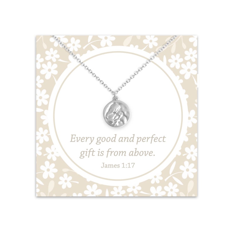 May include: Silver necklace with a round pendant featuring a textured image of two hands clasped together. The pendant is on a card with a white floral pattern and the text "Every good and perfect gift is from above. James 1:17"
