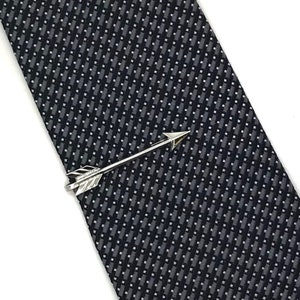 May include: Silver arrow tie clip with a textured finish. The clip is on a dark gray patterned tie.