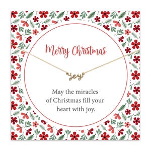 Może przedstawiać: Złoty naszyjnik ze słowem "joy" w kursywie jest prezentowany na świątecznej kartce. Karta ma czerwono-biały kwiatowy wzór z napisem "Merry Christmas" i świąteczną wiadomością.