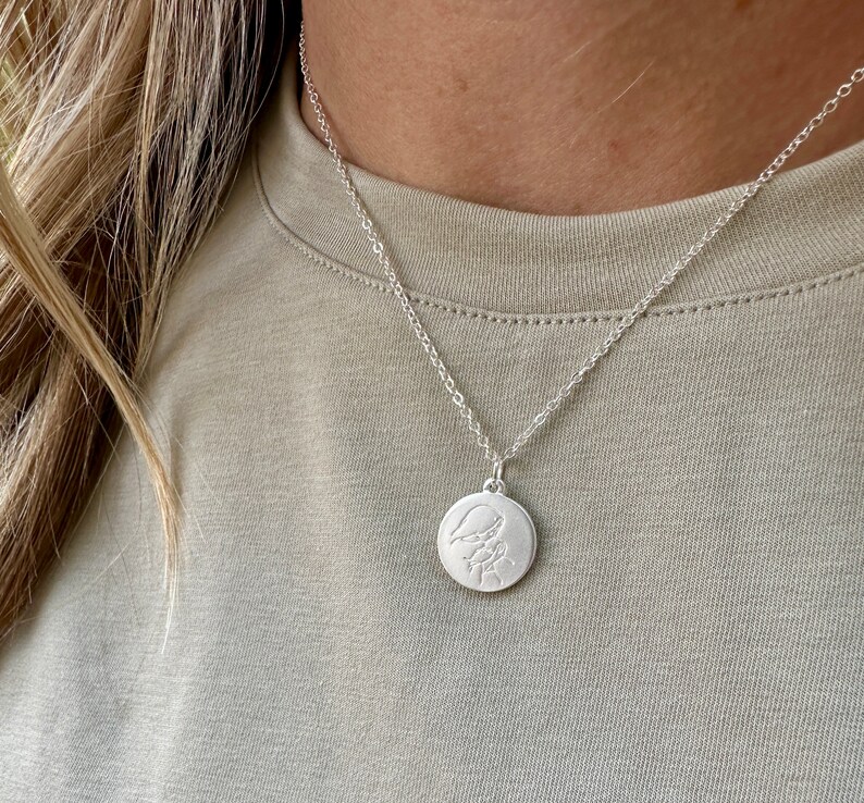 May include: A silver necklace with a round pendant featuring a delicate engraved design. The pendant is on a silver chain.