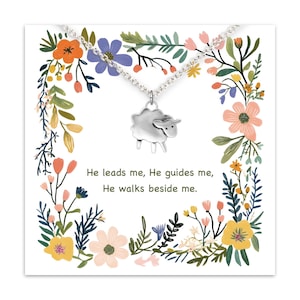 May include: A silver-toned sheep pendant necklace on a white card with floral illustrations. The card has text that reads, "He leads me, He guides me, He walks beside me." The floral border includes orange, pink, blue, and yellow flowers.