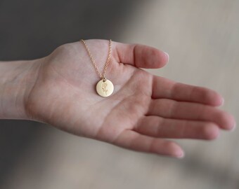 May include: A gold necklace with a delicate flower pendant. The pendant is a small, round disc with a floral design.