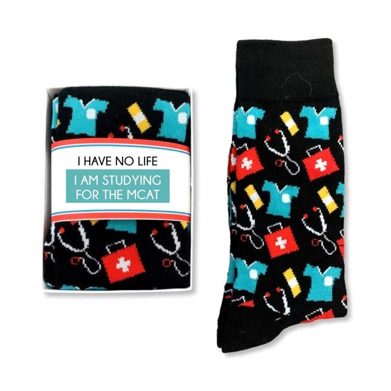 May include: A pair of black socks with a colorful pattern of medical symbols, including a stethoscope, a first aid kit, and a doctor's coat. The socks come in a box with the text "I have no life I am studying for the MCAT".