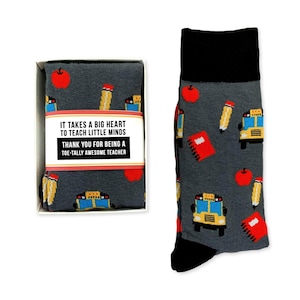 May include: A gift box containing a pair of gray socks with a school bus, apple, pencil, and notebook pattern. The box has a white label with the text "It takes a big heart to teach little minds. Thank you for being a toe-tally awesome teacher."