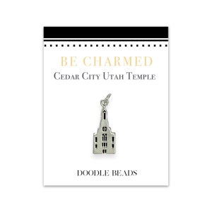 Puede incluir: Un charm de plata con un contorno detallado del Templo de Cedar City, Utah. El charm está en una tarjeta blanca con el texto "BE CHARMED" y "CEDAR CITY UTAH TEMPLE" en texto negro. La tarjeta también tiene el texto "DOODLE BEADS" en texto negro.