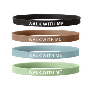 May include: Four silicone wristbands in black, brown, blue, and green. Each band has the white text "WALK WITH ME" printed across the front. The bands are a simple, classic design.