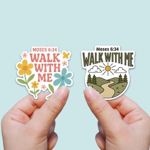 May include: Two stickers with the text "Walk With Me" from Moses 6:34. One sticker features flowers in yellow, orange, and blue. The other sticker shows a path, trees, and a sun. Both stickers are held up by a person.