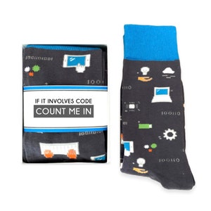 May include: A pair of black socks with a blue cuff. The socks feature a variety of computer-related icons, including a laptop, a lightbulb, a cloud, and a gear. The socks are packaged in a white box with the text "If it involves code count me in".