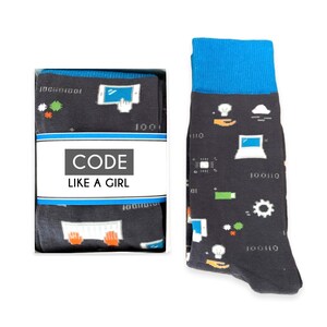 May include: A pair of black socks with a blue cuff. The socks feature a pattern of computer-related icons, including a keyboard, a computer mouse, a lightbulb, and a cloud. The socks also have the text "CODE LIKE A GIRL" on the box.
