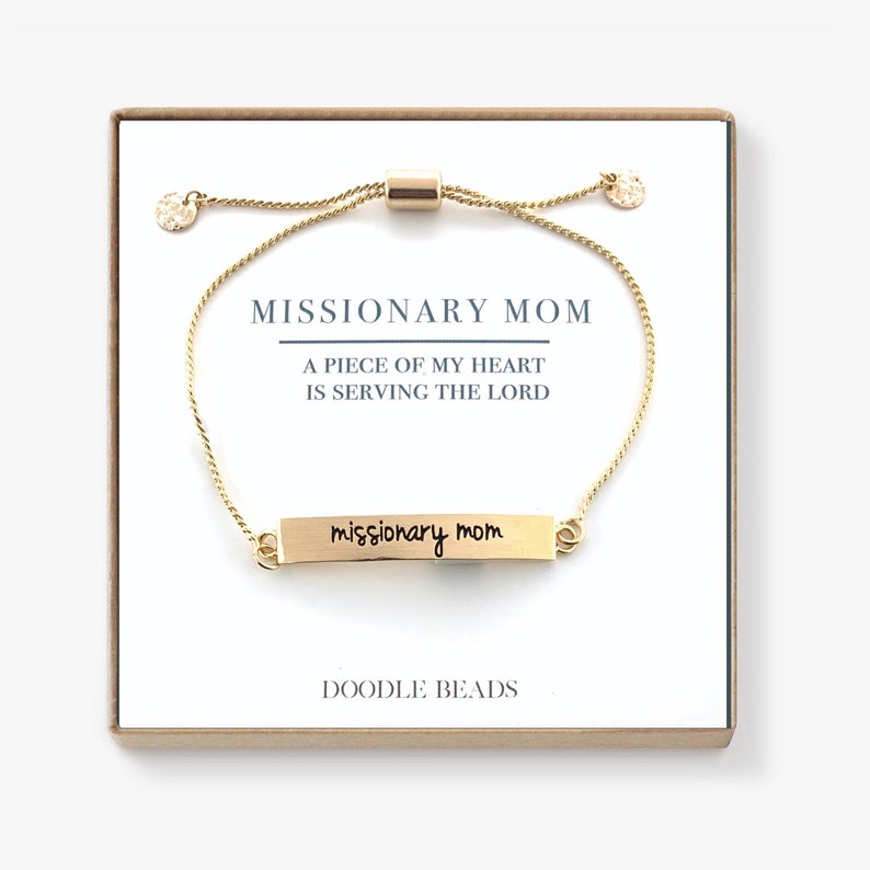 May include: Gold adjustable bracelet with a small rectangular charm that says "missionary mom" in cursive handwriting. The bracelet comes in a small box with the words "Missionary Mom, A piece of my heart is serving the Lord, Doodle Beads".