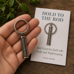 May include: A silver metal keychain with a rectangular pendant engraved with "HOLD TO THE ROD." The keychain is held in a hand next to a card with the same text and the phrase "And Flood the Earth with Truth and Righteousness."