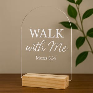 May include: Clear acrylic sign with an arched top, featuring the text "WALK with Me" and "Moses 6:34" in white. The sign is set on a rectangular wooden base, ideal for display on a desk or shelf.