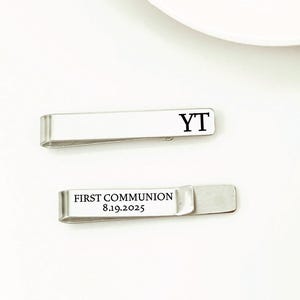 May include: Two silver tie clips with engraved text. The first tie clip says "YT" and the second tie clip says "FIRST COMMUNION 8.19.2025".
