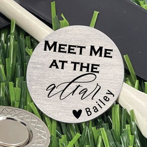 May include: A silver golf ball marker with the text "Meet me at the 19th" and a heart with the name "Bailey" engraved on it.