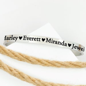 May include: A silver bracelet engraved with the names "Harley", "Everett", "Miranda", and "Jewel", separated by heart symbols.
