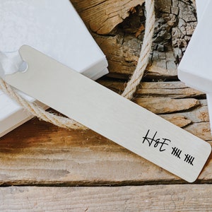 May include: A silver bookmark with a handwritten inscription that reads "H&E" followed by a series of hash marks.