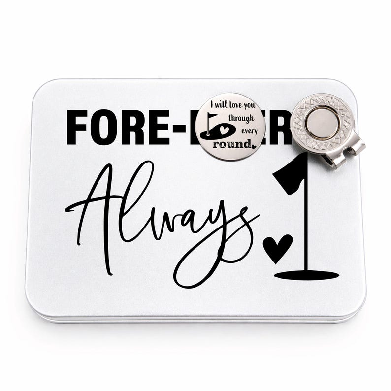 May include: A white golf ball marker tin with the words "FOREVER Always" in black. A golf ball marker with a flag and heart design is attached, along with a silver-colored golf ball marker clip.