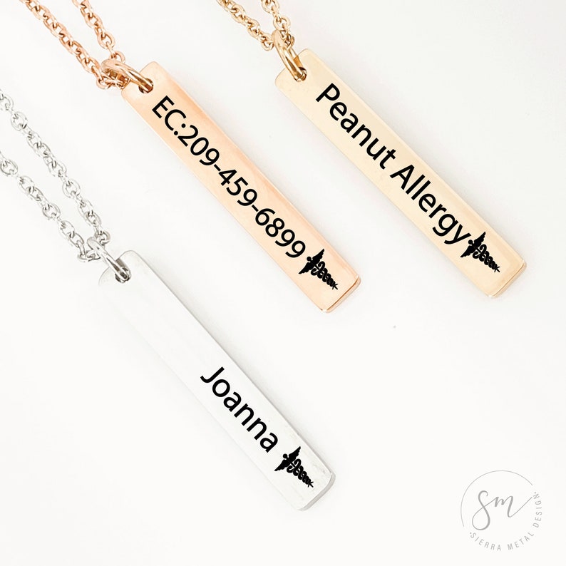 May include: Three silver, gold, and rose gold necklaces with vertical bar pendants. The pendants are engraved with the text "Peanut Allergy", "EC:209-459-6899", and "Joanna". Each pendant has a small medical symbol engraved on it.