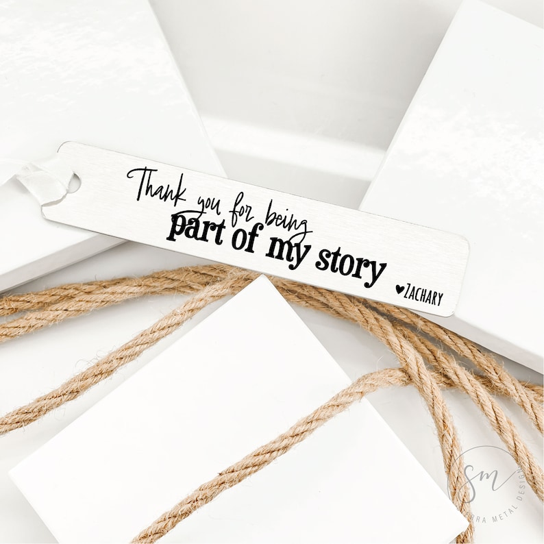 May include: A silver bookmark with the text "Thank you for being part of my story" and a heart symbol followed by the name "Zachary".