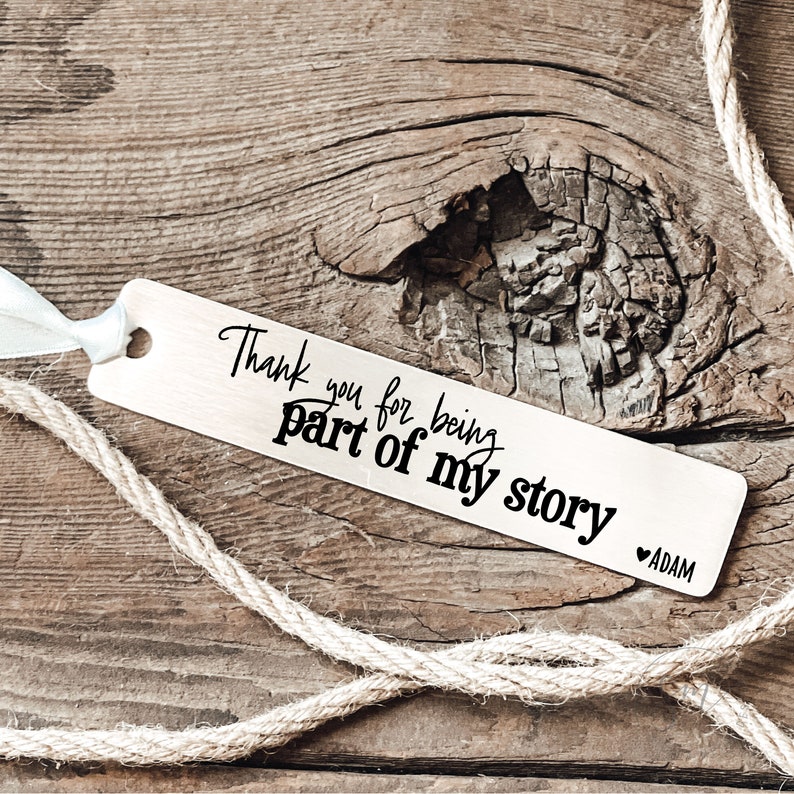 May include: Silver bookmark with the text "Thank you for being part of my story" and a heart with the name "ADAM" below.