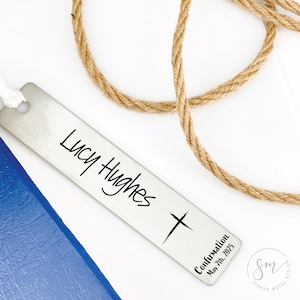 May include: Silver bookmark with a cross and the text "Lucy Hughes Confirmation May 7th, 2023".