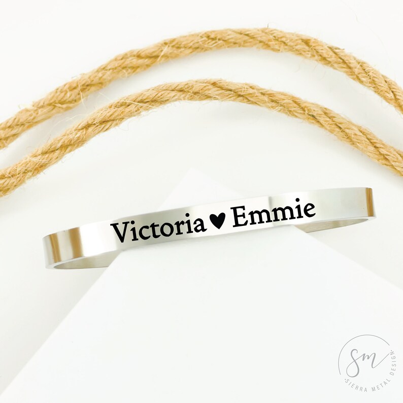 May include: A silver bangle bracelet engraved with the text "Victoria &hearts; Emme".