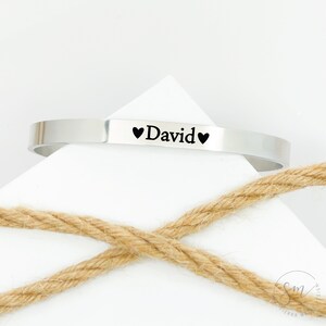 May include: A silver bangle bracelet engraved with the name "David" and two small hearts.