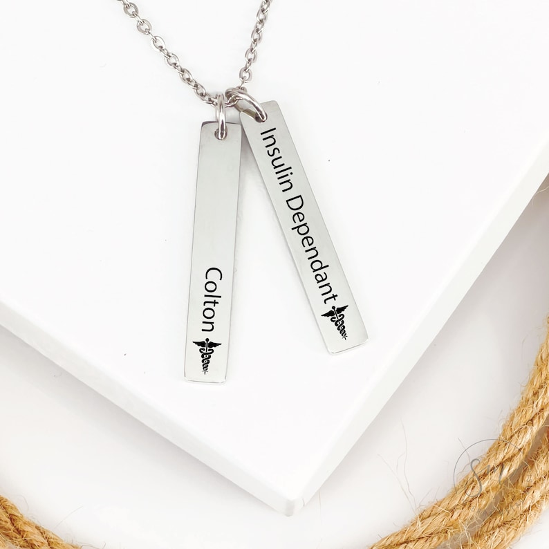 May include: Silver necklace with two vertical bars. The top bar reads "Insulin Dependant" with a medical symbol. The bottom bar reads "Colton" with a medical symbol.