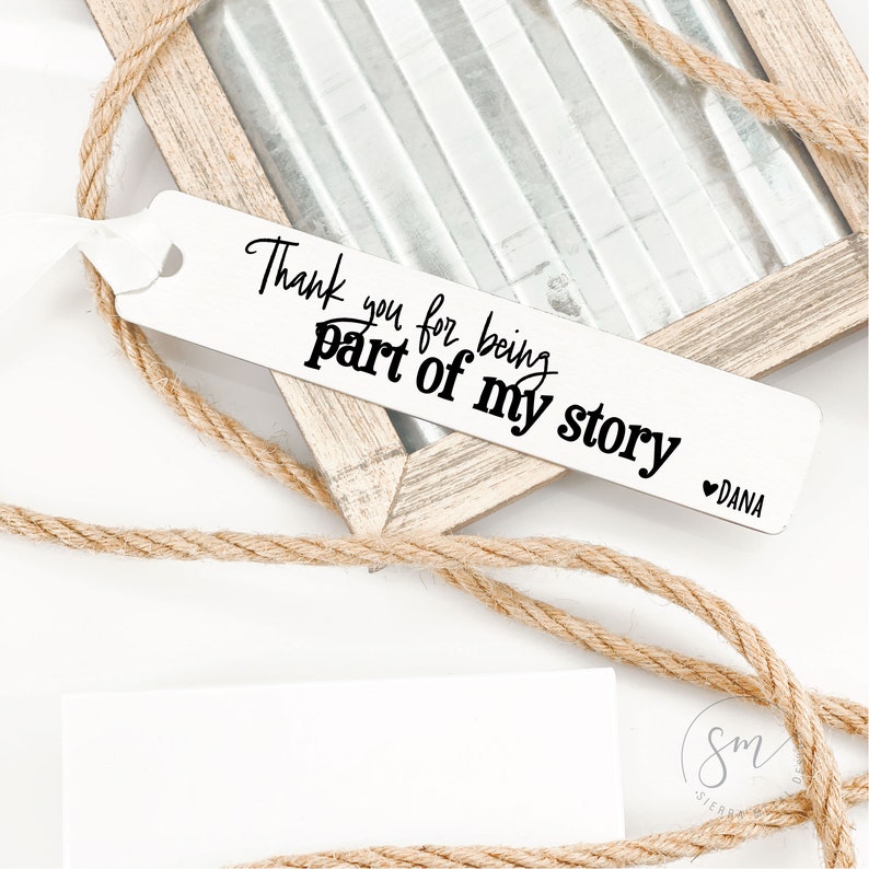 May include: White bookmark with black text that reads "Thank you for being part of my story" with a heart and the name "DANA" at the bottom.