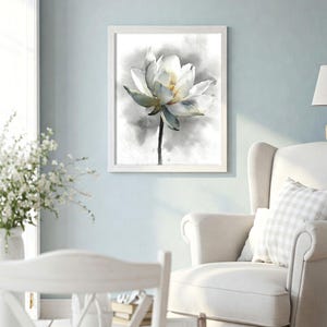 May include: A framed watercolor print of a white lotus flower. The flower has delicate petals with soft green and yellow accents, set against a gray and white background. The artwork is displayed in a white wooden frame.