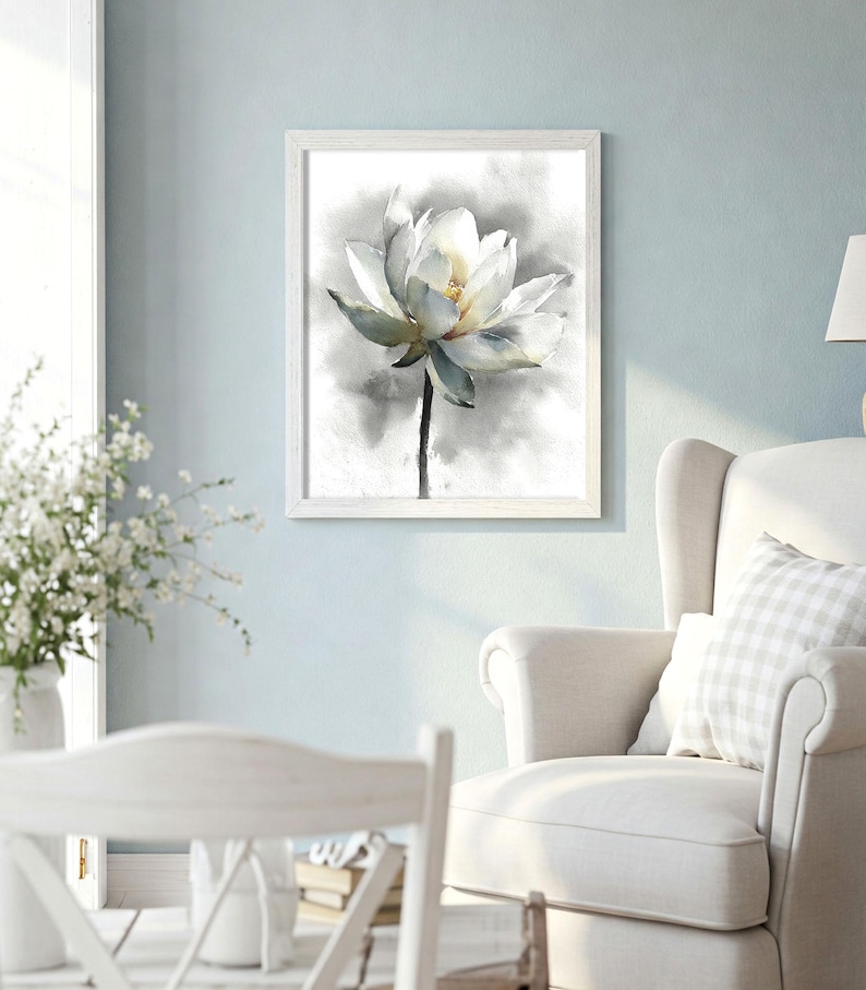 May include: A framed watercolor print of a white lotus flower. The flower has delicate petals with soft green and yellow accents, set against a gray and white background. The artwork is displayed in a white wooden frame.