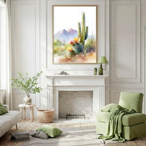 May include: Watercolor painting of a desert landscape with cacti and mountains. The artwork is framed in a light wood frame and hangs above a white fireplace. The room is decorated in neutral tones with green accents, including a sofa, chair, and pillows.