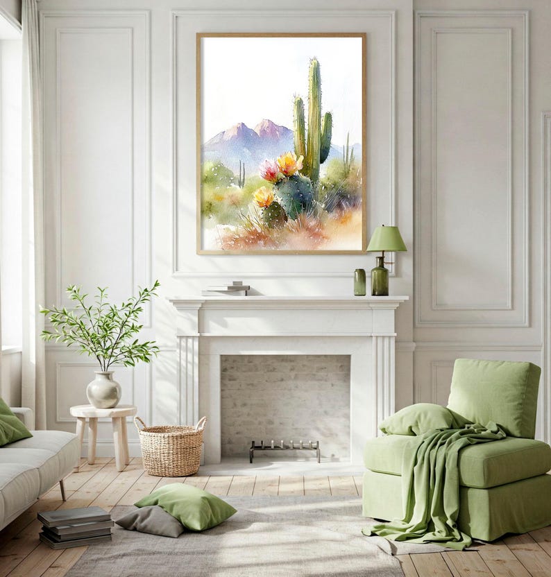 May include: Watercolor painting of a desert landscape with cacti and mountains. The artwork is framed in a light wood frame and hangs above a white fireplace. The room is decorated in neutral tones with green accents, including a sofa, chair, and pillows.