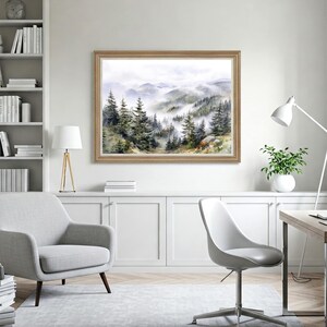 May include: A framed watercolor painting of a misty mountain landscape with evergreen trees. The artwork is in a light brown wooden frame and hangs above a white cabinet. The room features a gray armchair, a white chair, and a floor lamp.