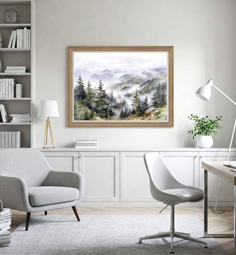 May include: A framed watercolor painting of a misty mountain landscape with evergreen trees. The artwork is in a light brown wooden frame and hangs above a white cabinet. The room features a gray armchair, a white chair, and a floor lamp.