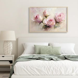 May include: A framed floral painting featuring pink roses with green leaves. The artwork is set against a soft, textured background with a light wooden frame. The painting is displayed above a bed with white linens and green pillows.